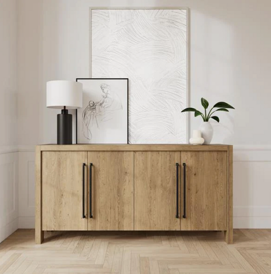 A light brown buffet with black handles, a black lamp, and a plant