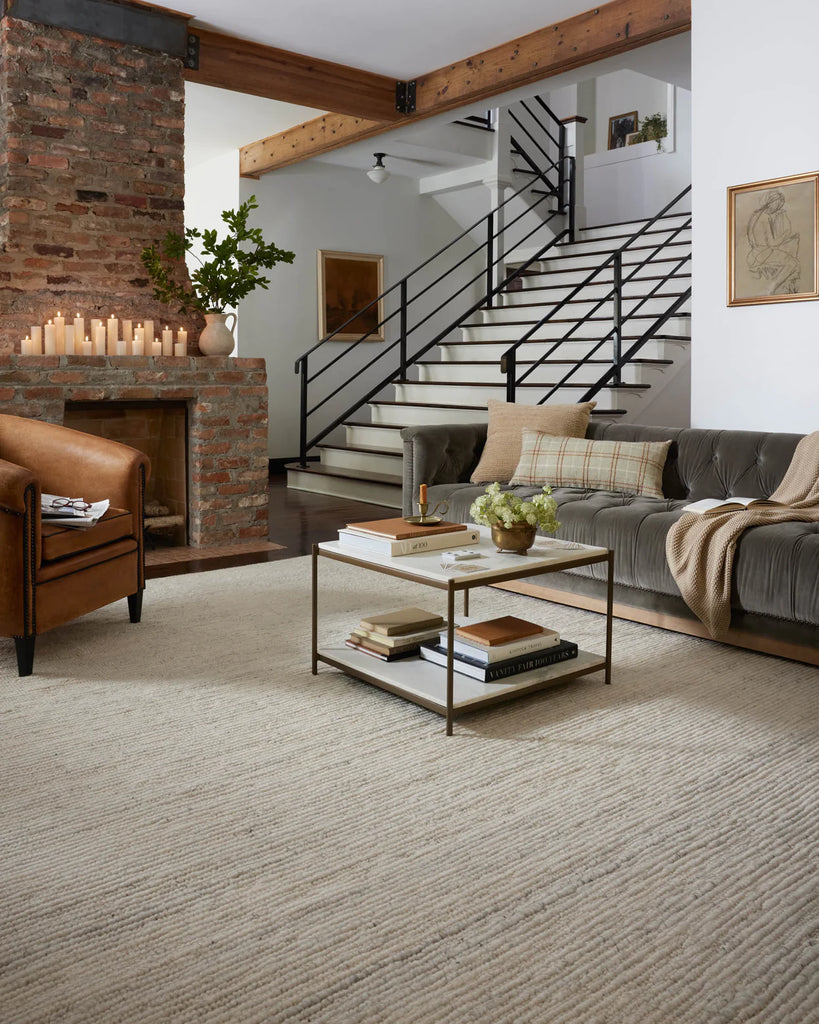 A cozy gray couch, light-colored rug, white coffee table, and brown chair 