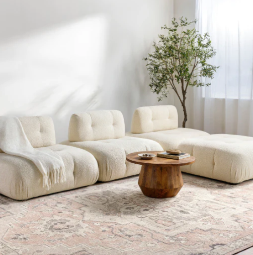 A white seating arrangement, round wooden table, and intricate rug