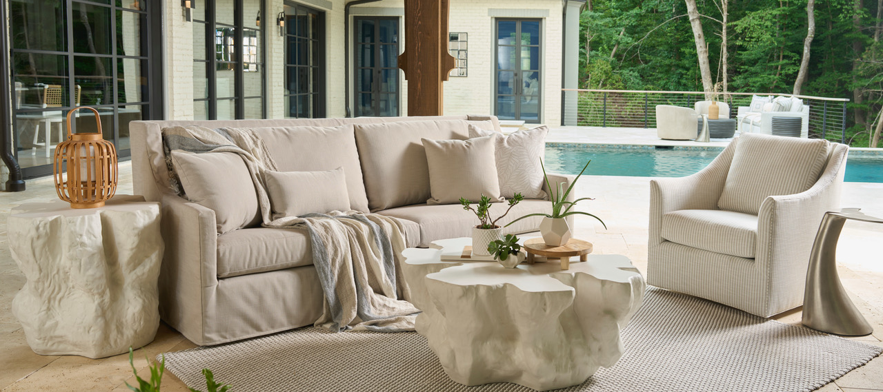 Outdoor patio with beige sofa, armchair, and coffee table by a poolside.